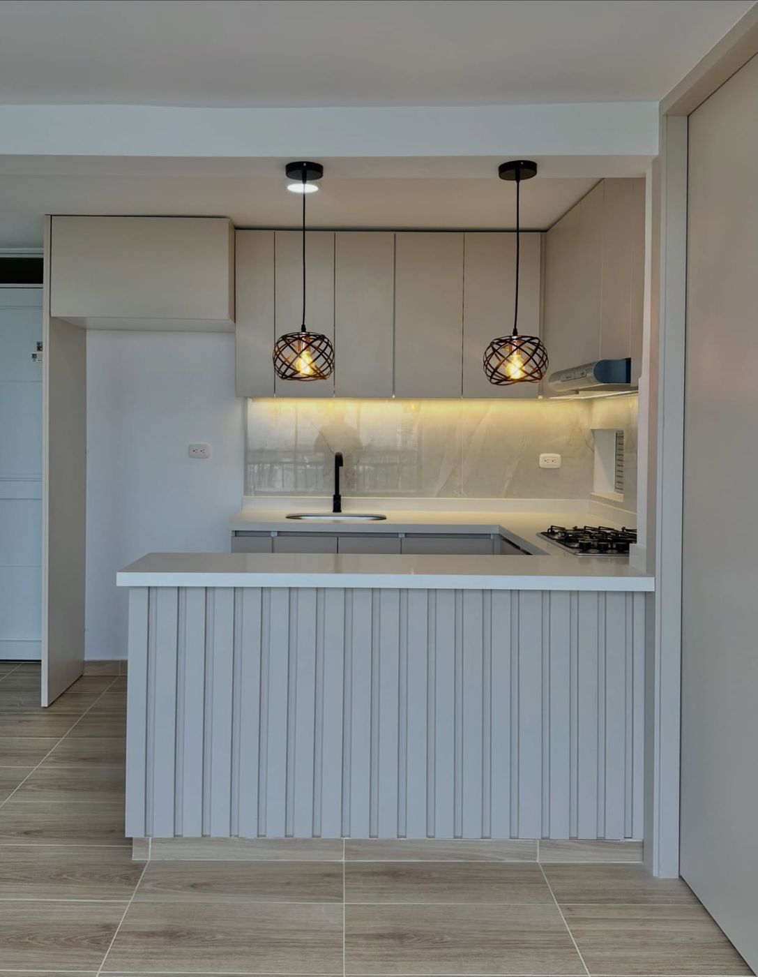 Cocina de apartamento remodelada, con gabinetes color arena y mesón blanco