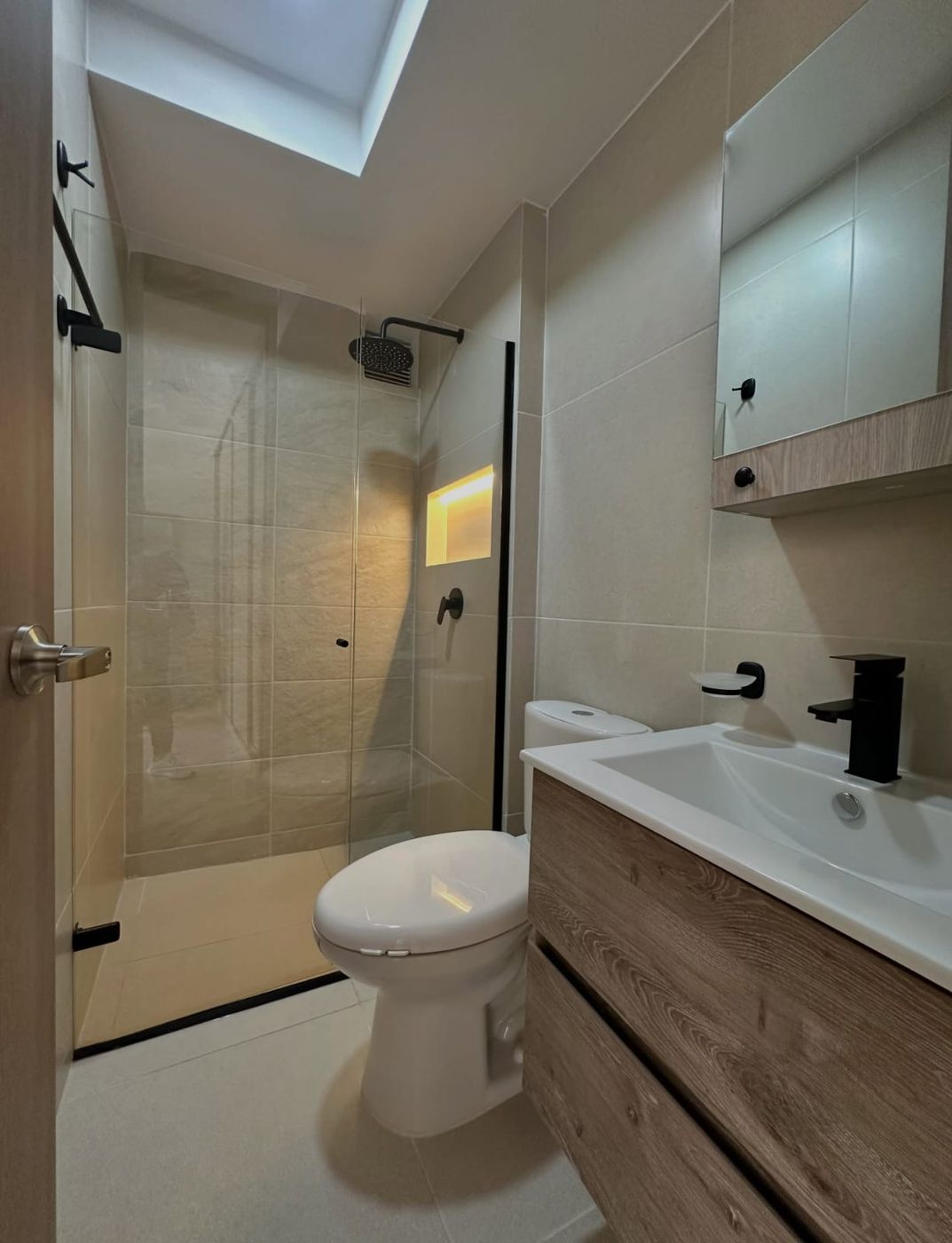 Baño de apartamento remodelado, con ducha de vidrio y mueble en madera